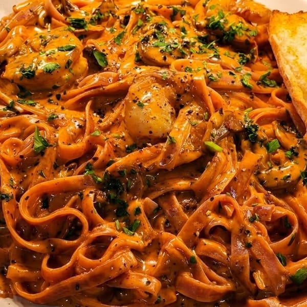 Creamy orange pasta with mushrooms and herbs, served with a slice of garlic bread.