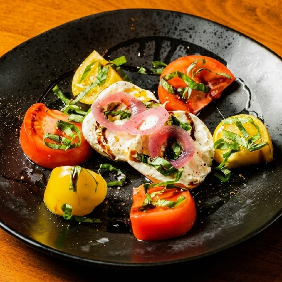 Caprese salad with red and yellow tomatoes, mozzarella, basil, red onion, and balsamic glaze.